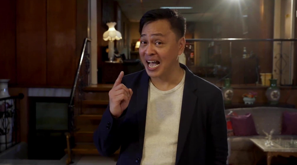 Ned Legaspi passionately delivering a speech, dressed in a navy blazer and white shirt, with an expressive gesture in a warmly lit indoor setting.