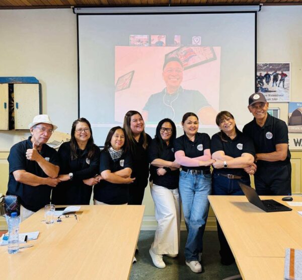 Members of the Filipino Correspondent Network gather for a group photo in The Hague while Ned Legaspi joins them virtually on a large screen.