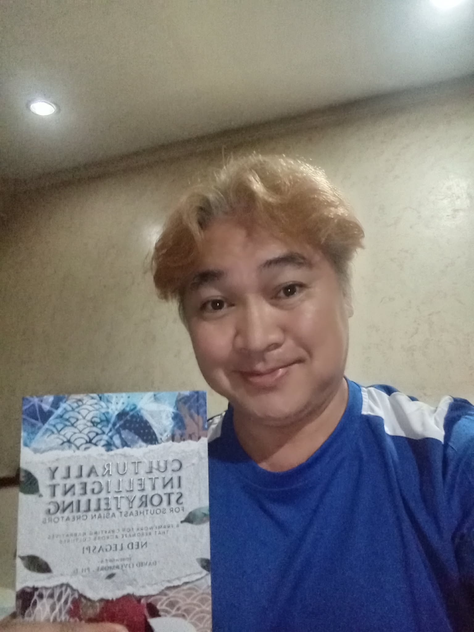 Oliver Rucio smiling while holding a copy of Culturally Intelligent Storytelling for Southeast Asian Creators